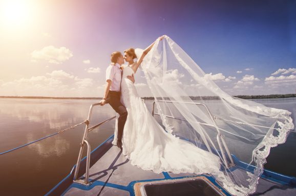 Hochzeitspaar auf einem Boot, Braut mit Schleier im Sonnenlicht, schöner klarer Himmel.