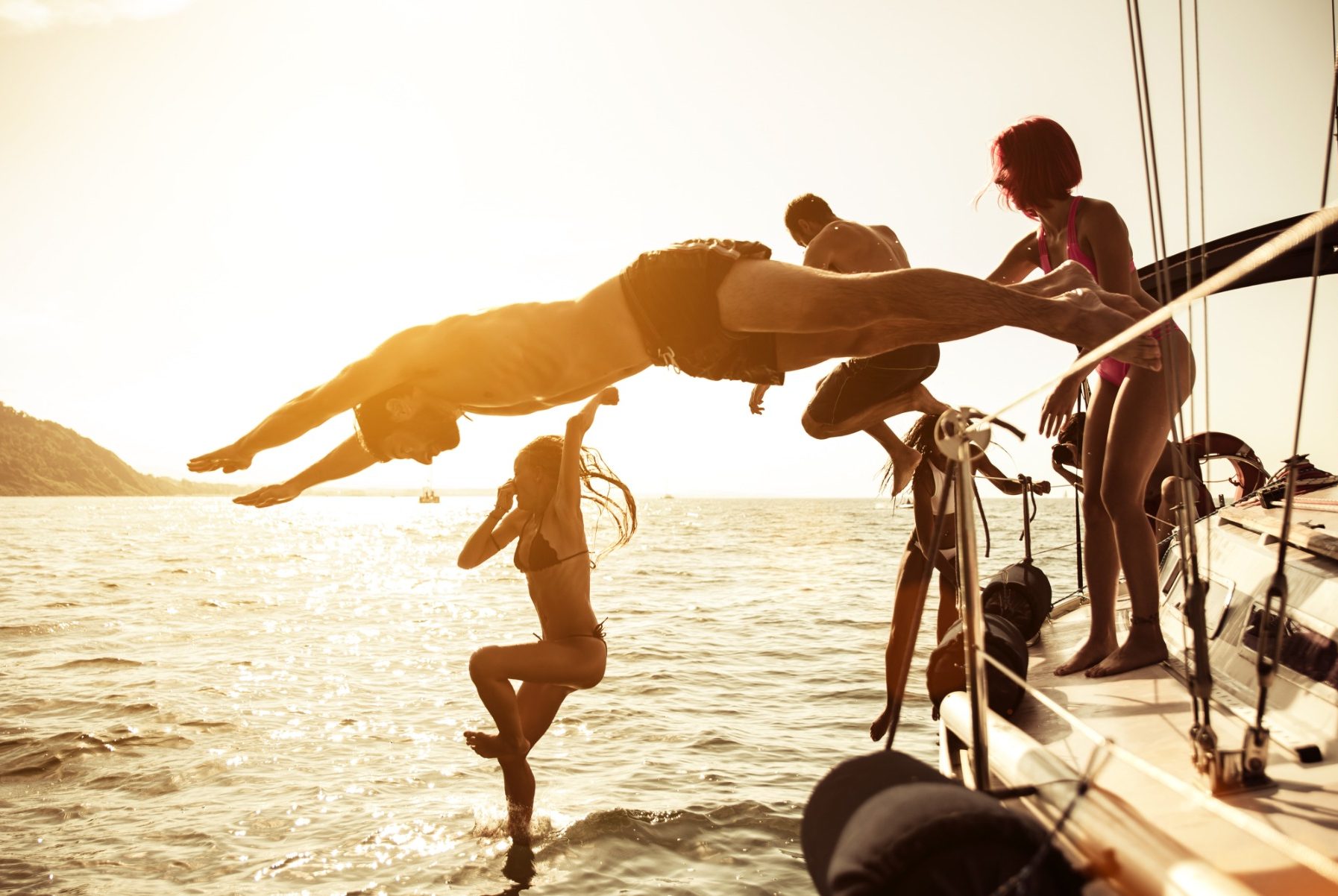 Gruppenszene mit Personen, die von einem Boot ins Wasser springen, im Sonnenuntergang.
