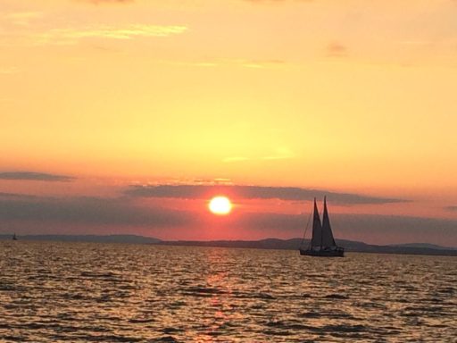 Segelboot auf dem Wasser vor einem Sonnenuntergang mit orangefarbenem Himmel.